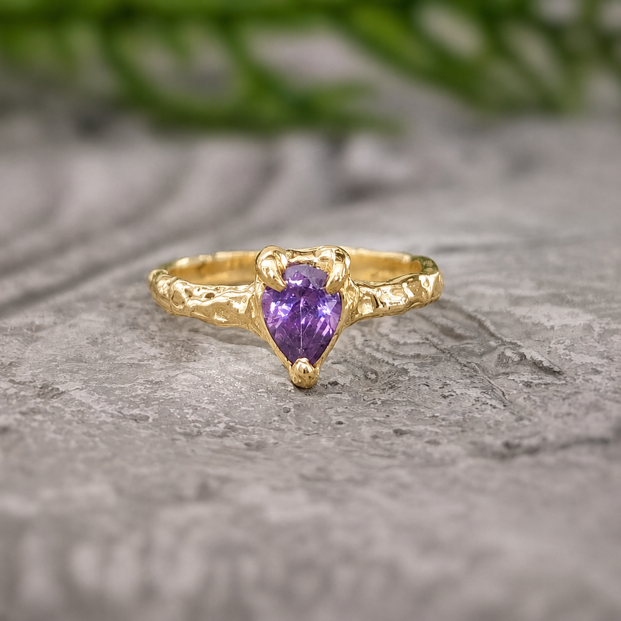 Gold ring with a purple heart-shaped gemstone on a stone surface