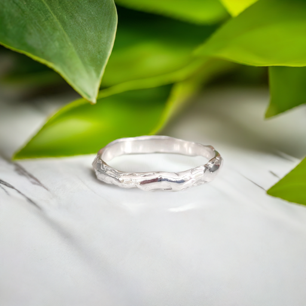 Molten Silver wedding band displayed among green leaves, showcasing its elegant organic texture and unique handcrafted design.