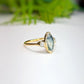 Side view Gold Moss Agate and raw diamond engagement ring in a light background with some greenery