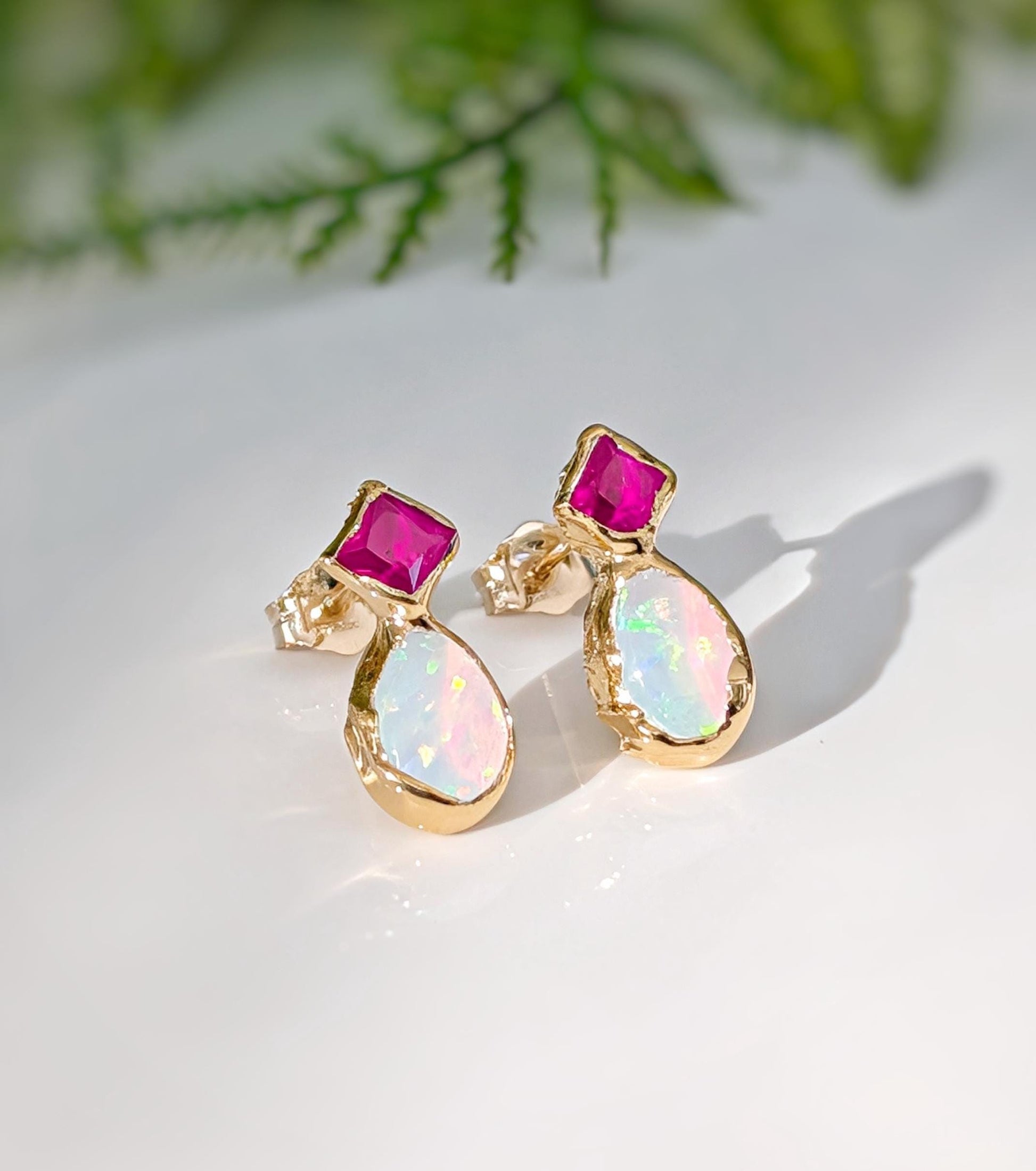 Pair of Gold stud earrings with dark pink Rubies and White Opals on a light background