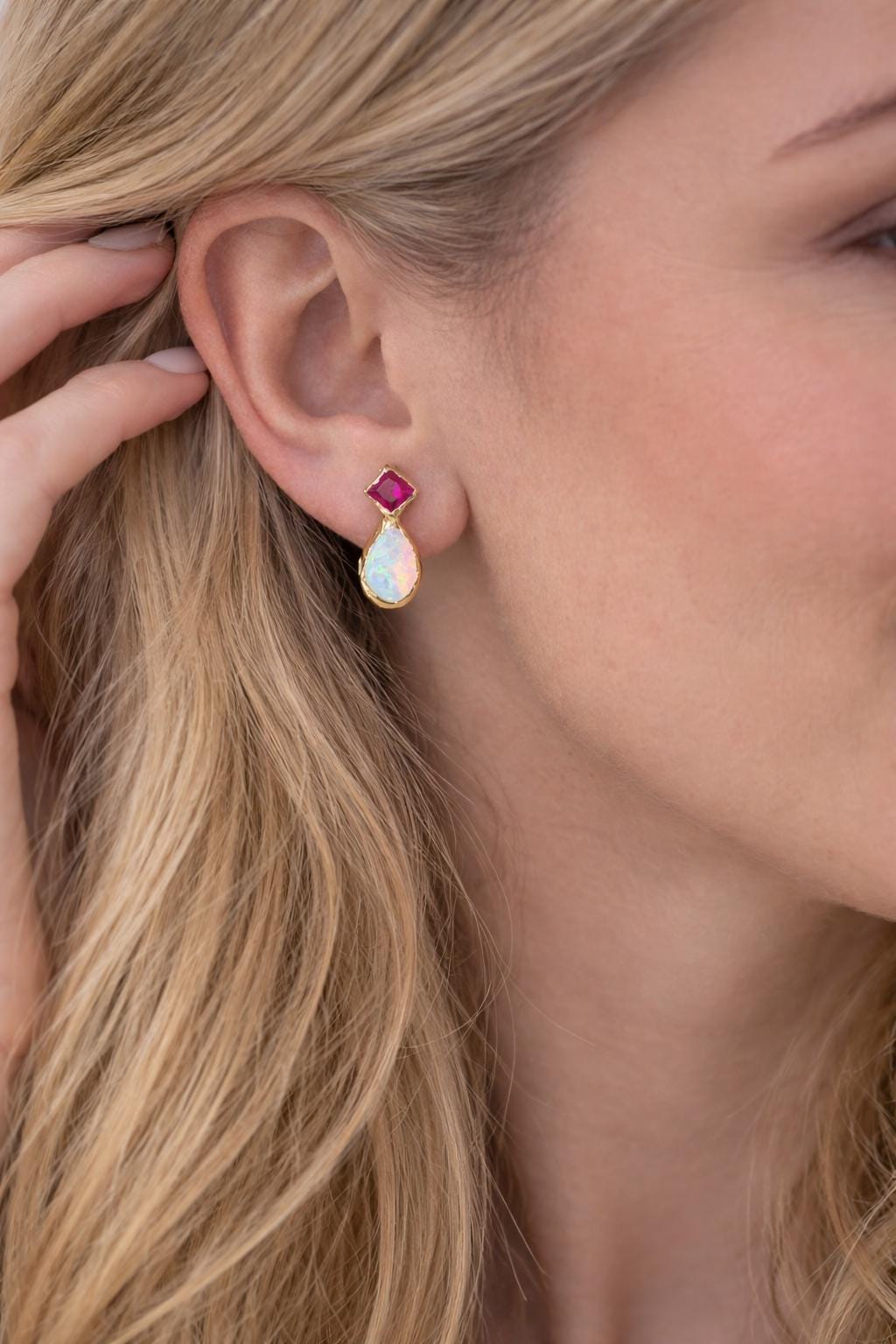 A blond woman wearing a Pair of Gold stud earrings with dark pink Rubies and White Opals