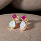 Gold earrings with pink gemstones and opal-like stones on a stone surface