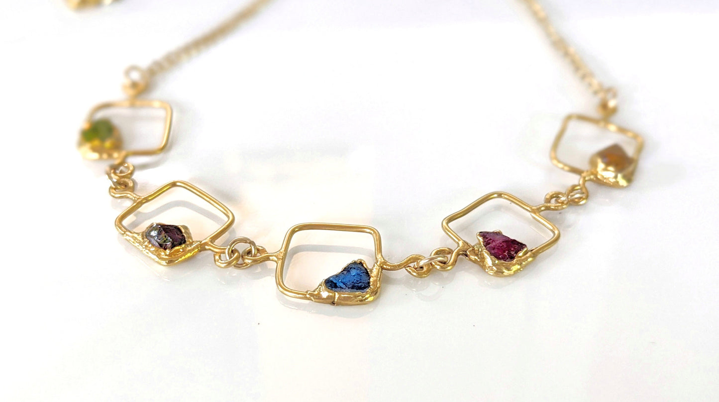 Close-up of personalized family birthstone necklace with raw gemstones and gold accents on square pendants.