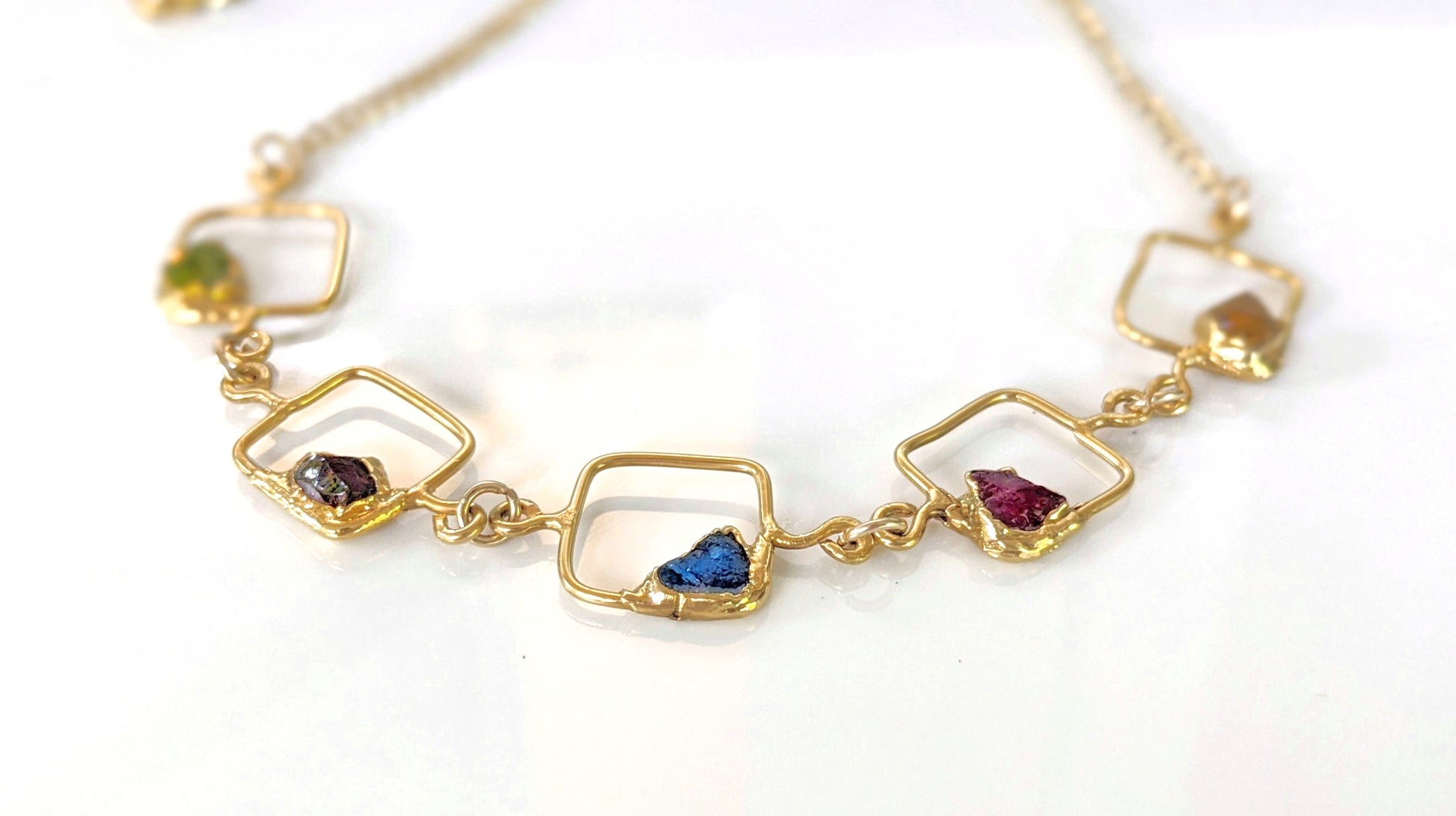 Close-up of personalized family birthstone necklace with raw gemstones and gold accents on square pendants.