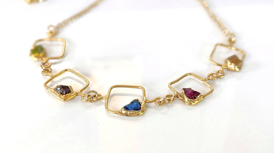 Close-up of personalized family birthstone necklace with raw gemstones and gold accents on square pendants.