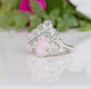 Silver ring with a pink Morganite as central stone and raw diamonds on a white surface with green leaves in the background