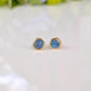 A pair of gold stud earrings with raw blue Montana Sapphires, placed on a white surface.