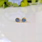 A pair of gold stud earrings with raw blue Montana Sapphires, placed on a white surface.