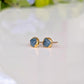 A pair of gold stud earrings with raw blue Montana Sapphires, placed on a white surface.