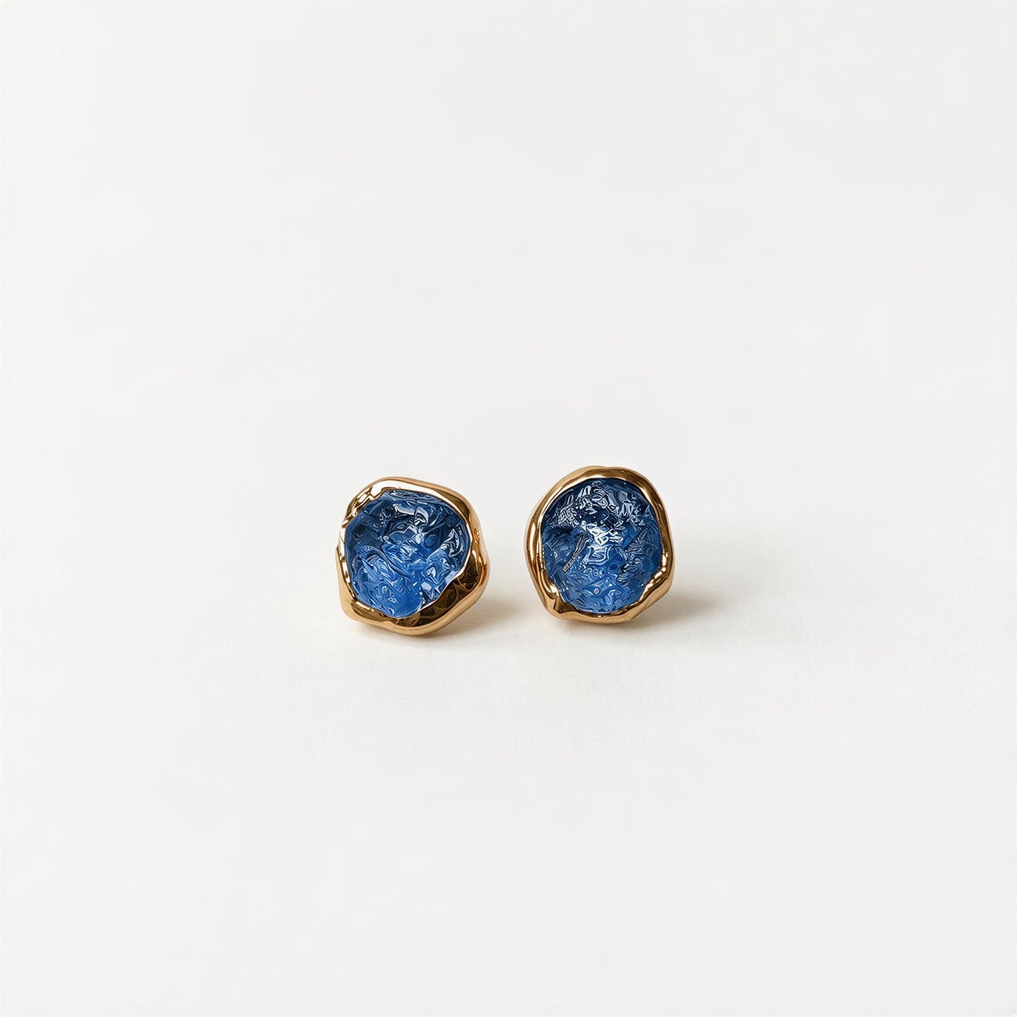 A pair of gold earrings with raw blue Montana Sapphires, placed on a white background.