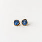 A pair of gold earrings with raw blue Montana Sapphires, placed on a white background.