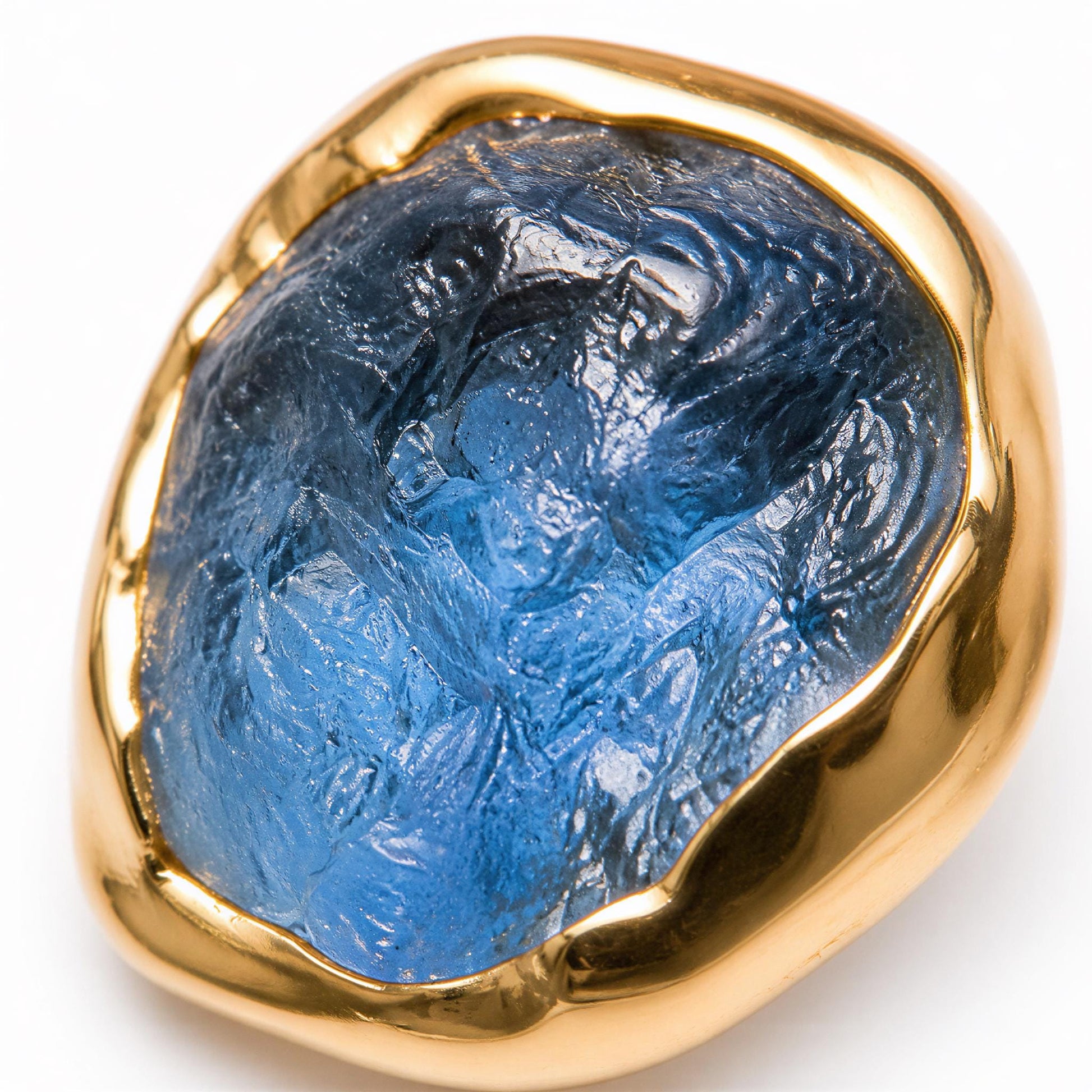 A close-up image of a raw blue Montana Sapphire stud earring set in a textured gold bezel, set against a white background.