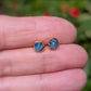 A hand holding a pair of small, raw Teal blue Montana Sapphire stud earrings.