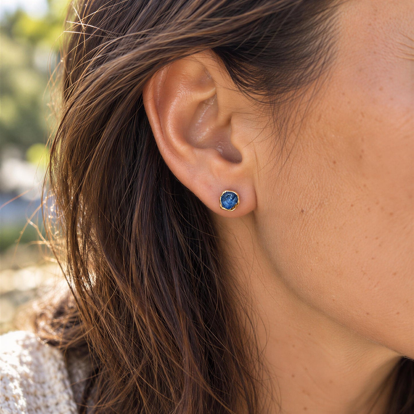 A close-up view of a person's ear adorned with a raw blue Montana Sapphire stud earring.