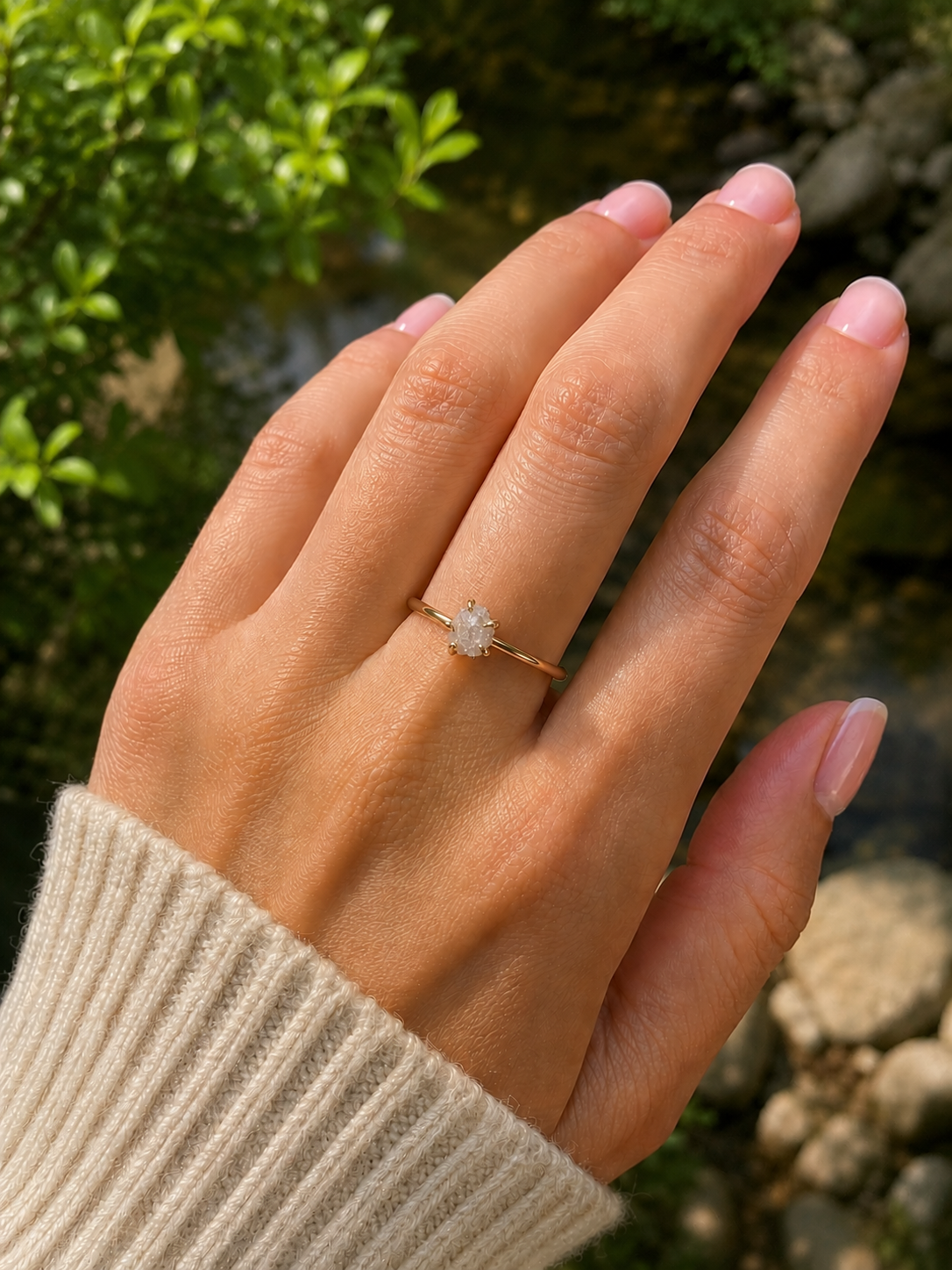 Hand wearing a raw diamond ring with a green outdoor background