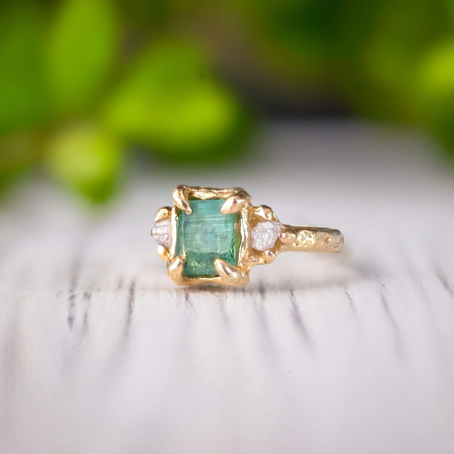 Raw emerald and diamond engagement ring in solid 14k gold, showcasing a mint green emerald and two small diamonds.