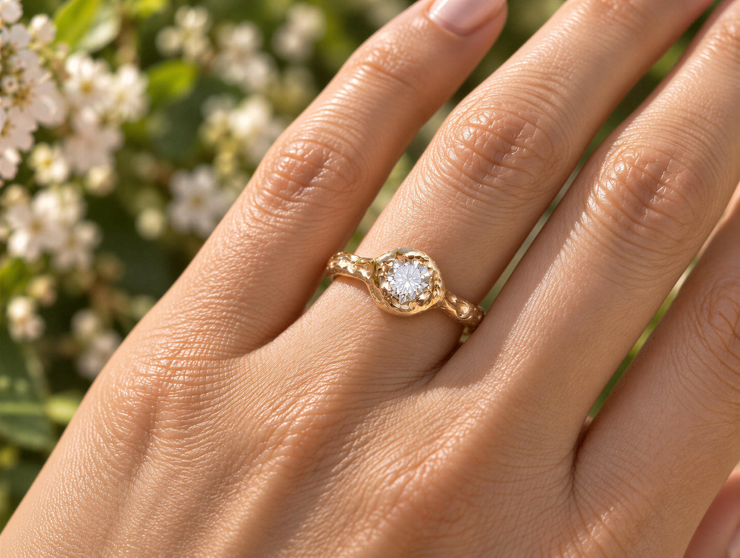 A close-up of a gold-textured engagement ring featuring a round Moissanite set in the center, worn on a woman's hand.