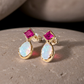 Gold earrings with a dark pink Ruby and opal gemstones on a stone surface