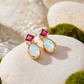 Gold stud earrings with Ruby and Opal gemstones on a stone surface