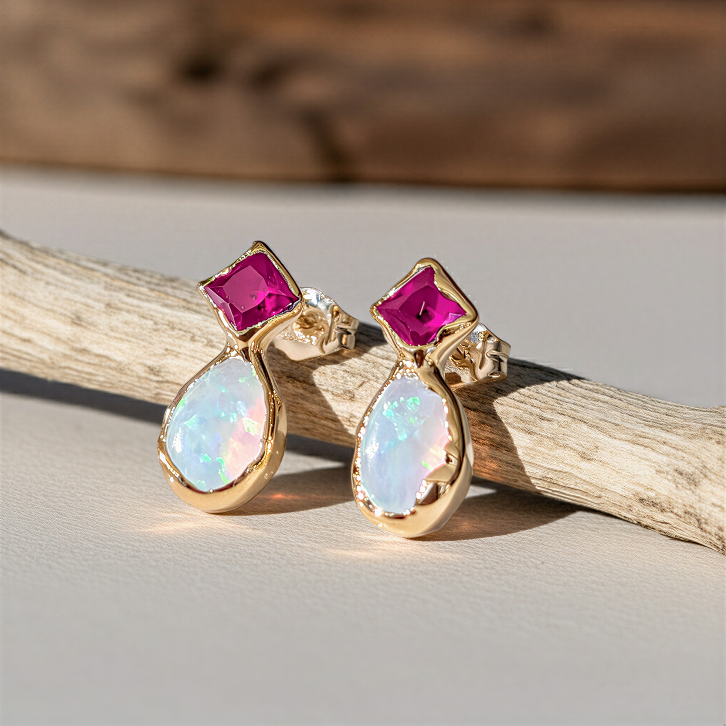 Gold earrings with Ruby and opal gemstones sitting on a branch