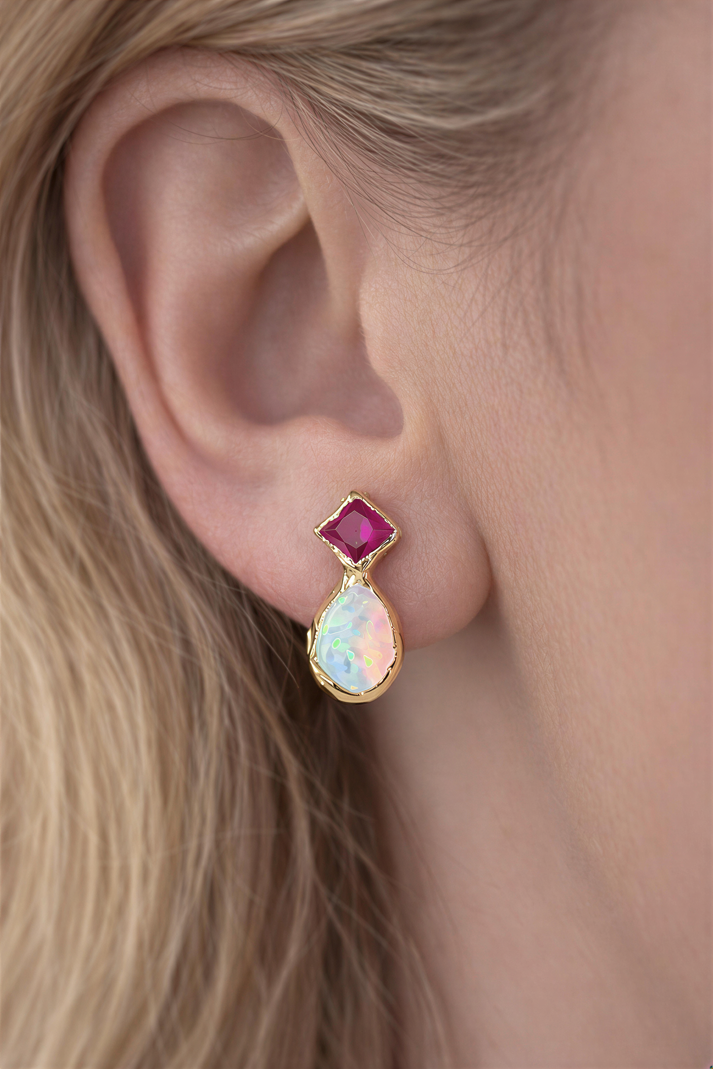 Close-up of a woman wearing a Pair of Gold stud earrings with dark pink Rubies and White Opals