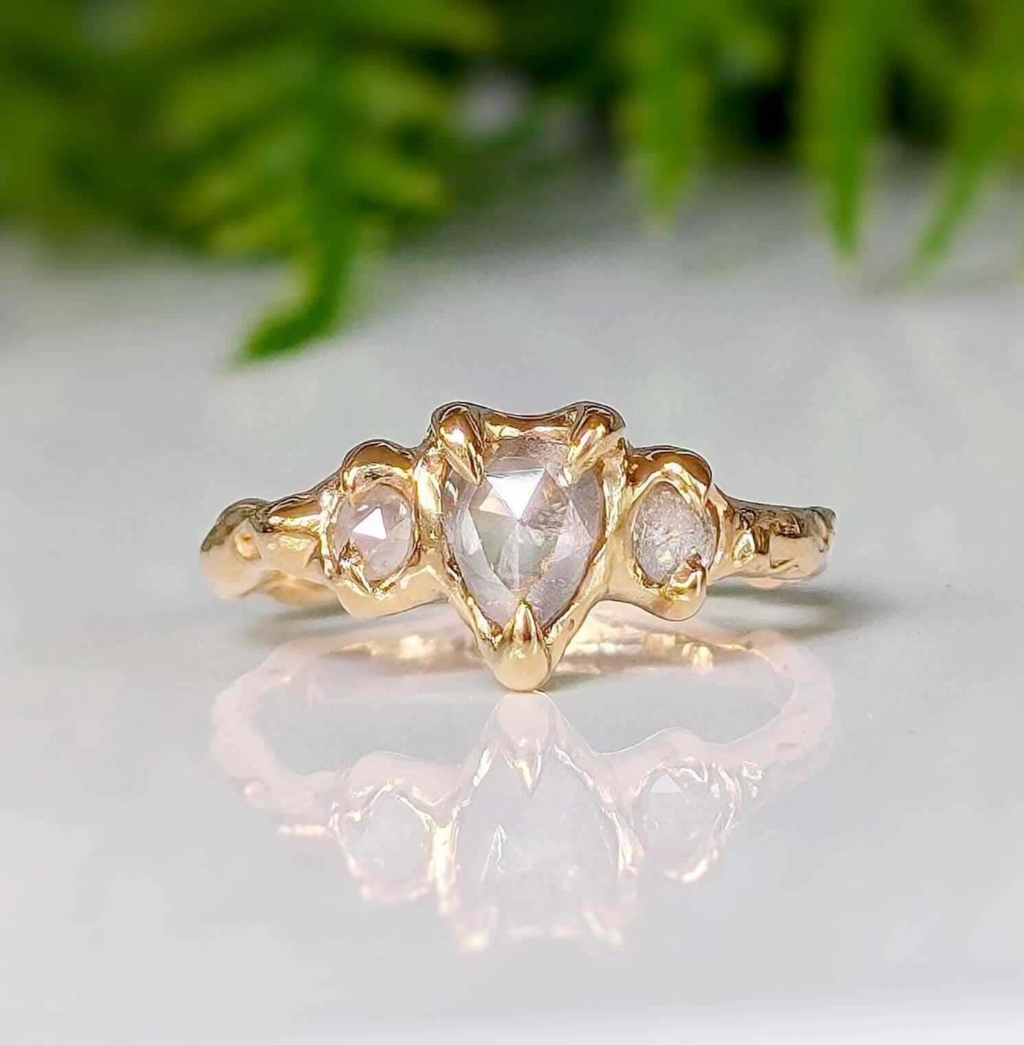 Rustic solid gold engagement ring featuring a pearl-shaped diamond and two smaller stones, ideal for a unique proposal.