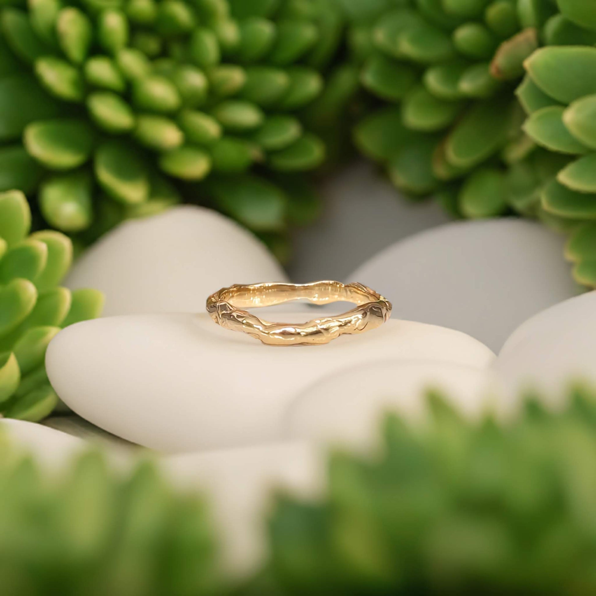 Molten textured Gold wedding band surrounded by succulent plants and white stones
