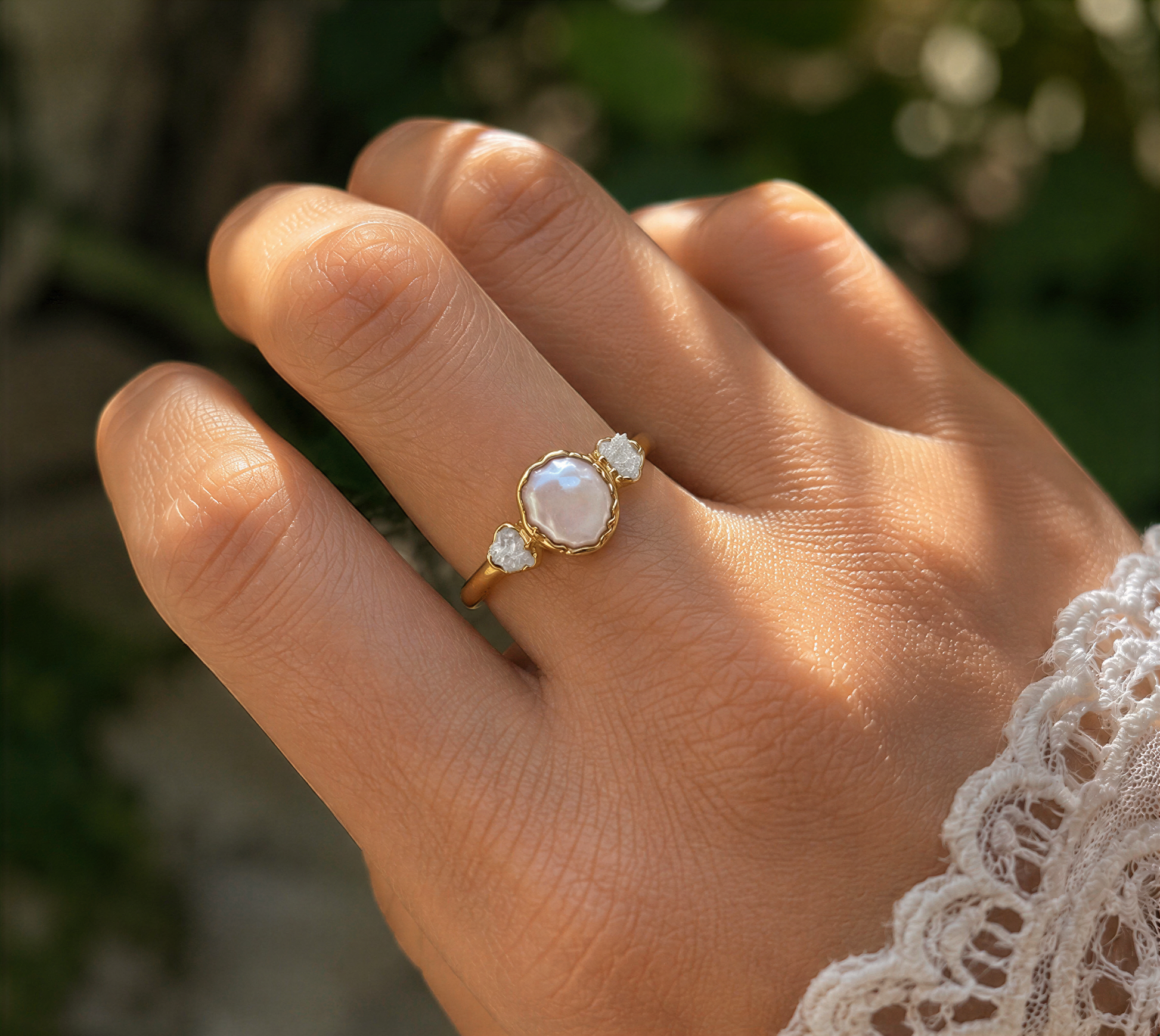 A close-up of a hand wearing a gold ring with a pearl and three diamonds.