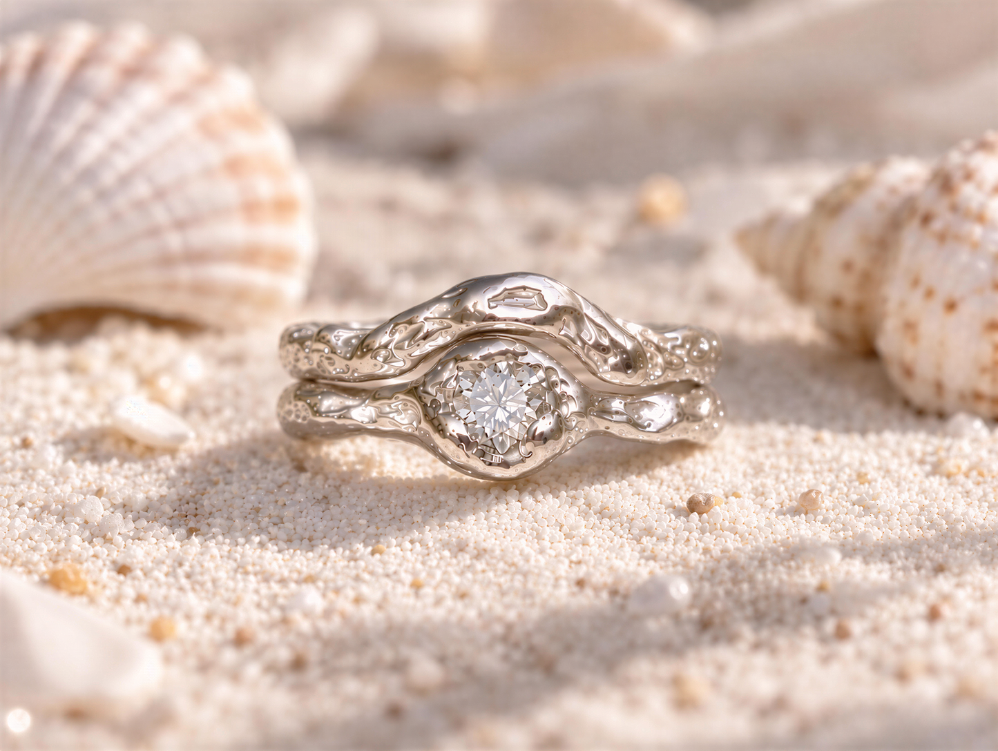 A silver ring with a large diamond set in the center, surrounded by a smaller ring, rests on a sandy beach.