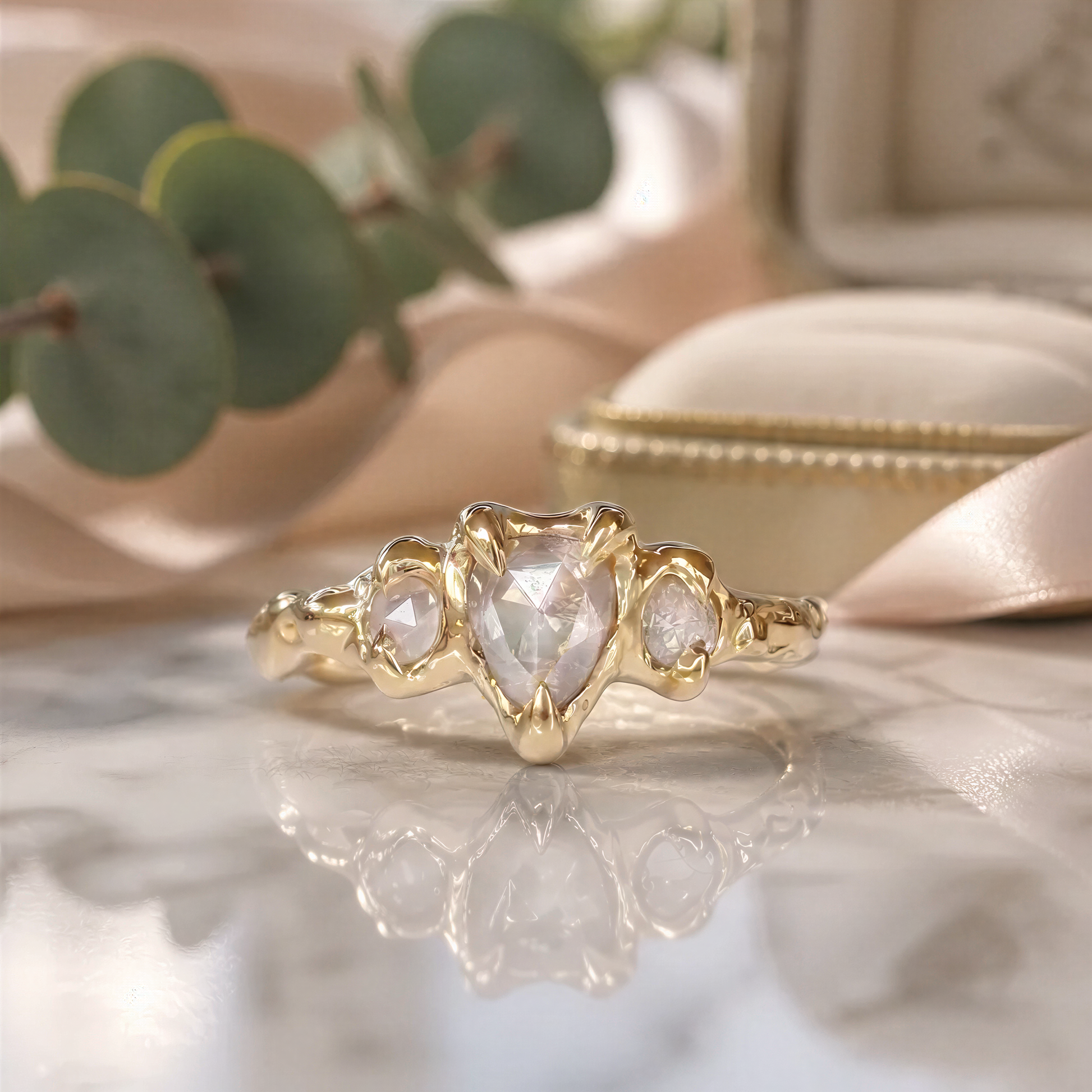 A gold ring with a large diamond in the center, surrounded by smaller diamonds, sits on a marble surface with a green plant in the background.