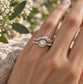 A close-up of a person's hand wearing a silver ring with a large diamond set in the center.