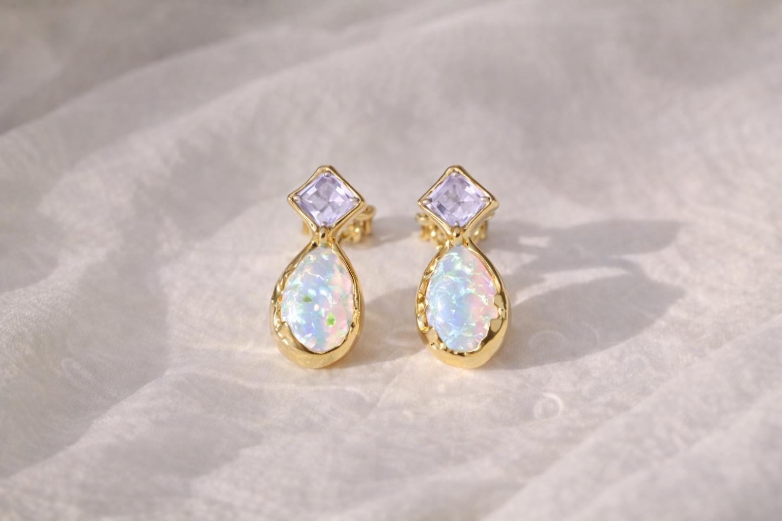 Pair of gold stud earrings with Amethysts and opal gemstones on a textured beige surface