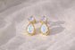 Pair of gold stud earrings with Amethysts and opal gemstones on a textured beige surface