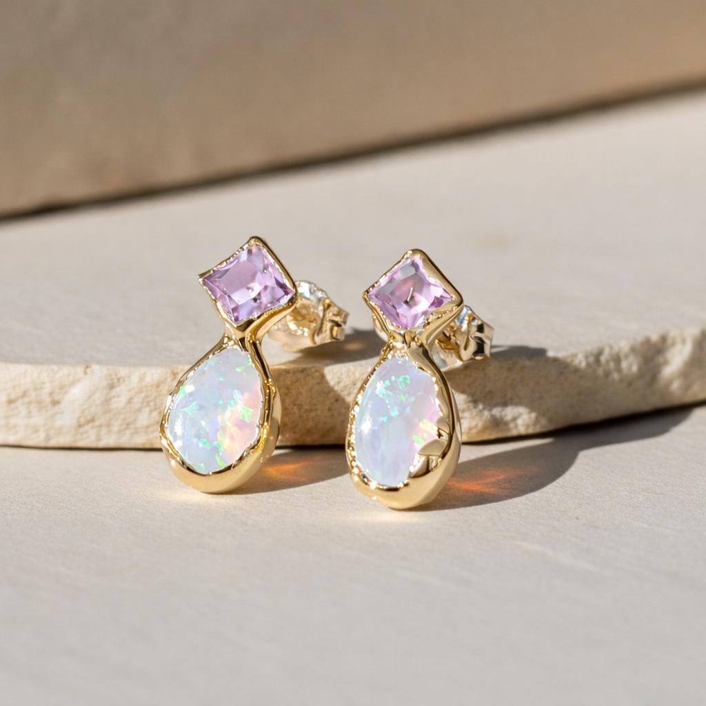 Gold earrings with pink and white gemstones on a beige surface
