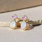 Gold earrings with pink and white gemstones on a beige surface