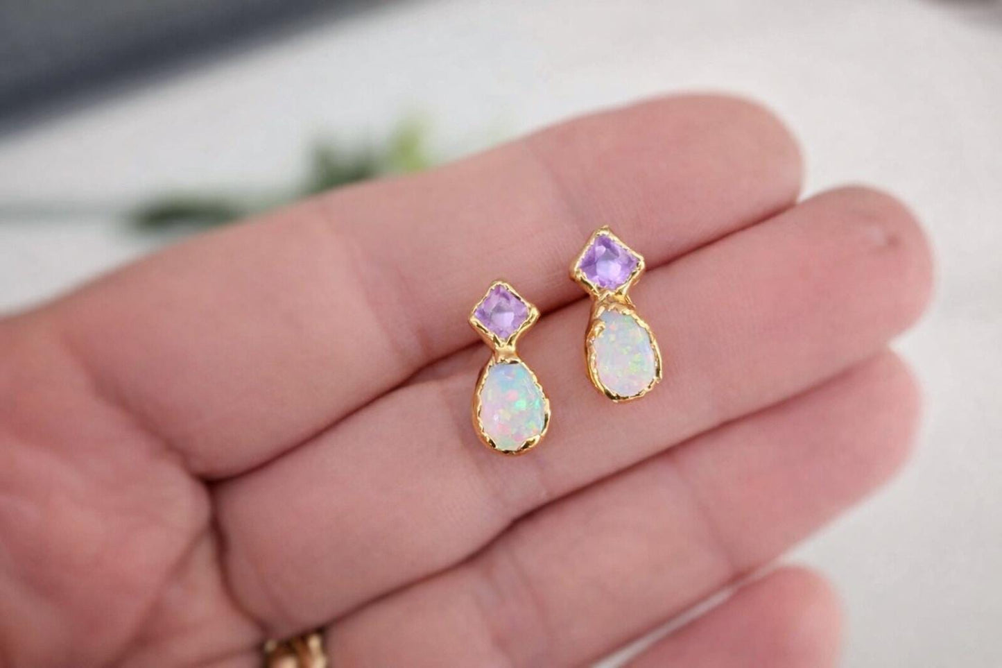 Opal and Amethyst gemstone stud earrings held in a hand with a blurred background