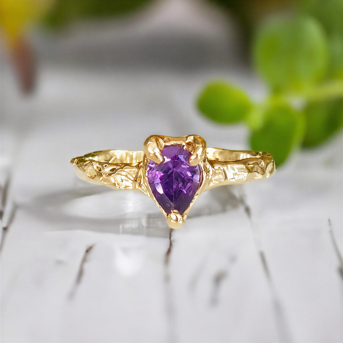 A Solid 14k Gold textured ring featuring a pear-shaped amethyst - set on a white wooden surface