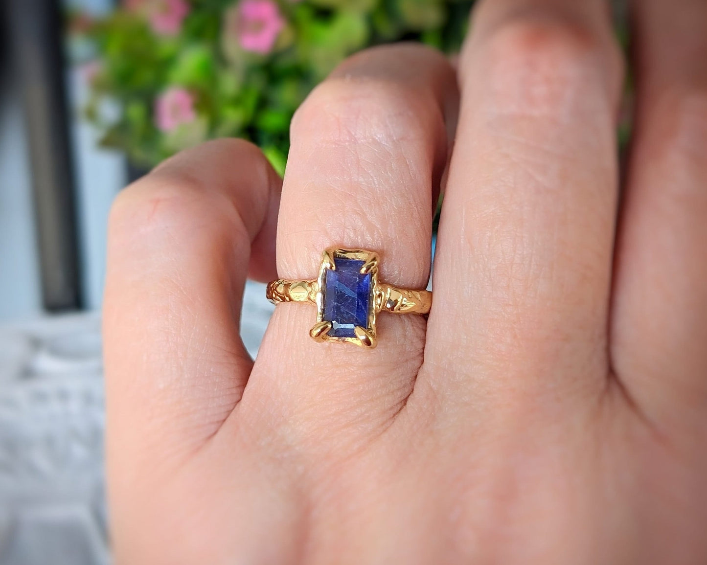 Hand wearing a blue sapphire ring in gold, featuring an emerald cut stone and intricate band design.