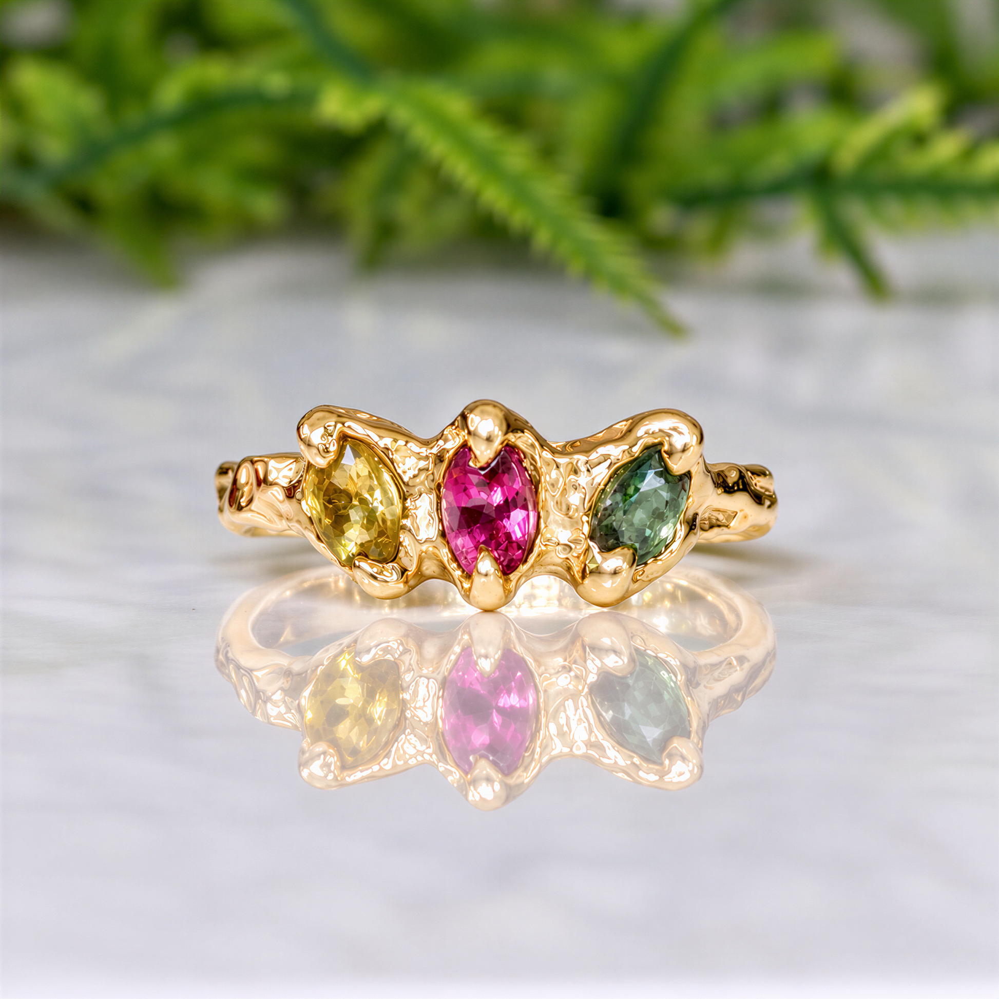 A gold ring with three gemstones, two pink and one green, set in a unique design.
