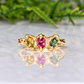 A gold ring with three gemstones, two pink and one green, set in a unique design.