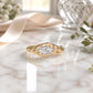 A gold ring with a large diamond set in the center, resting on a marble surface.