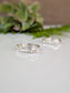 Two silver rings with a central stone are displayed on a white surface, with a blurred green plant in the background.
