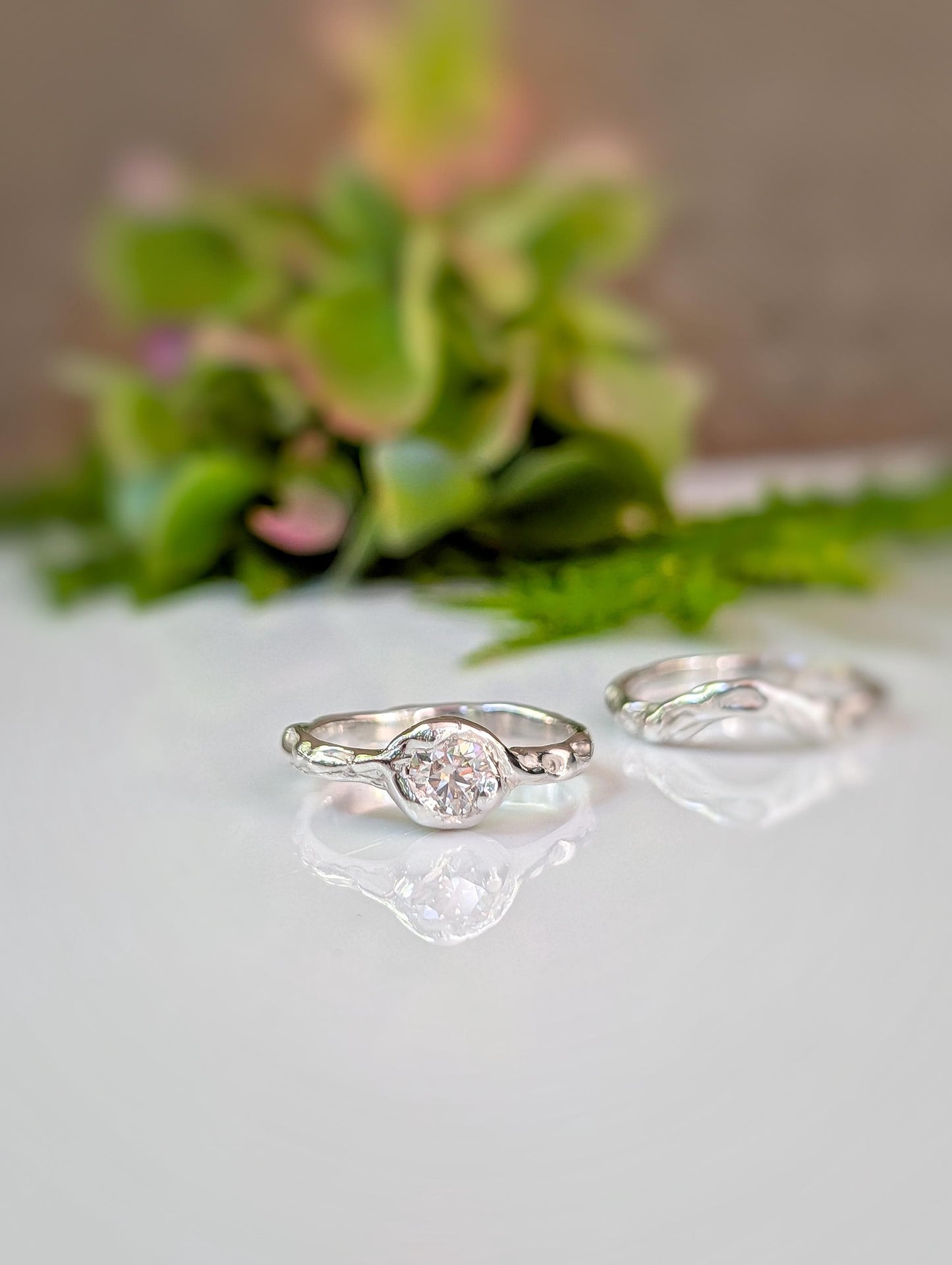 two silver rings with a large central stone, placed on a white surface with a blurred green plant in the background.