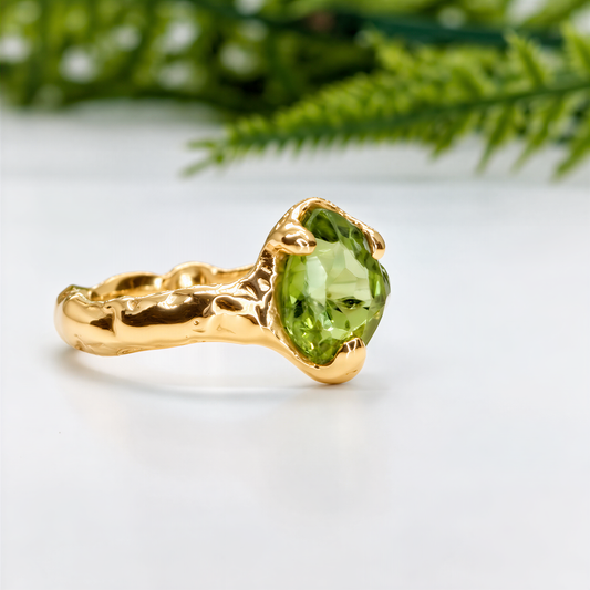 A gold ring with a large, vibrant green gemstone, likely an emerald, set in a textured band.