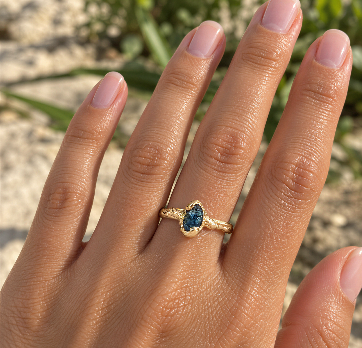 A close-up of a person's hand wearing a gold ring with a blue gemstone.
