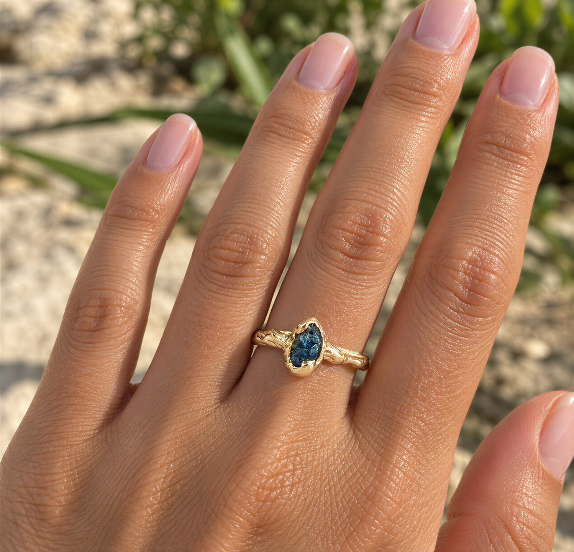A close-up of a person's hand wearing a gold ring with a blue gemstone.