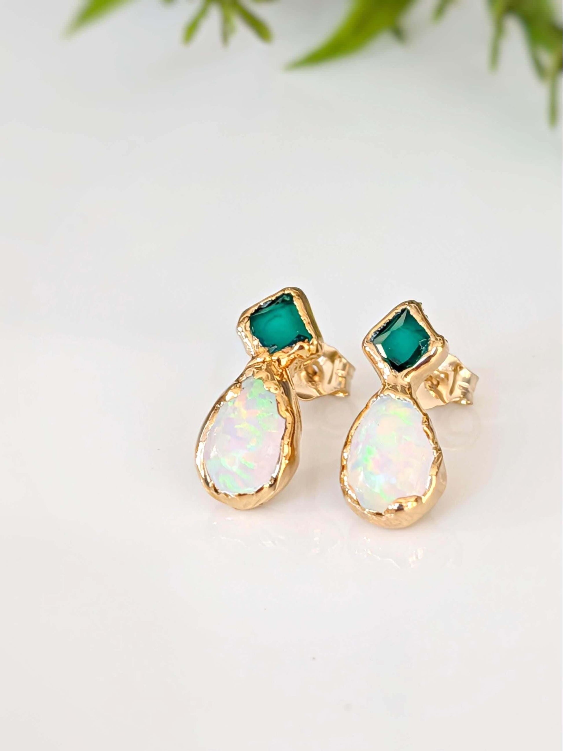Gold earrings with green and white gemstones on a light background