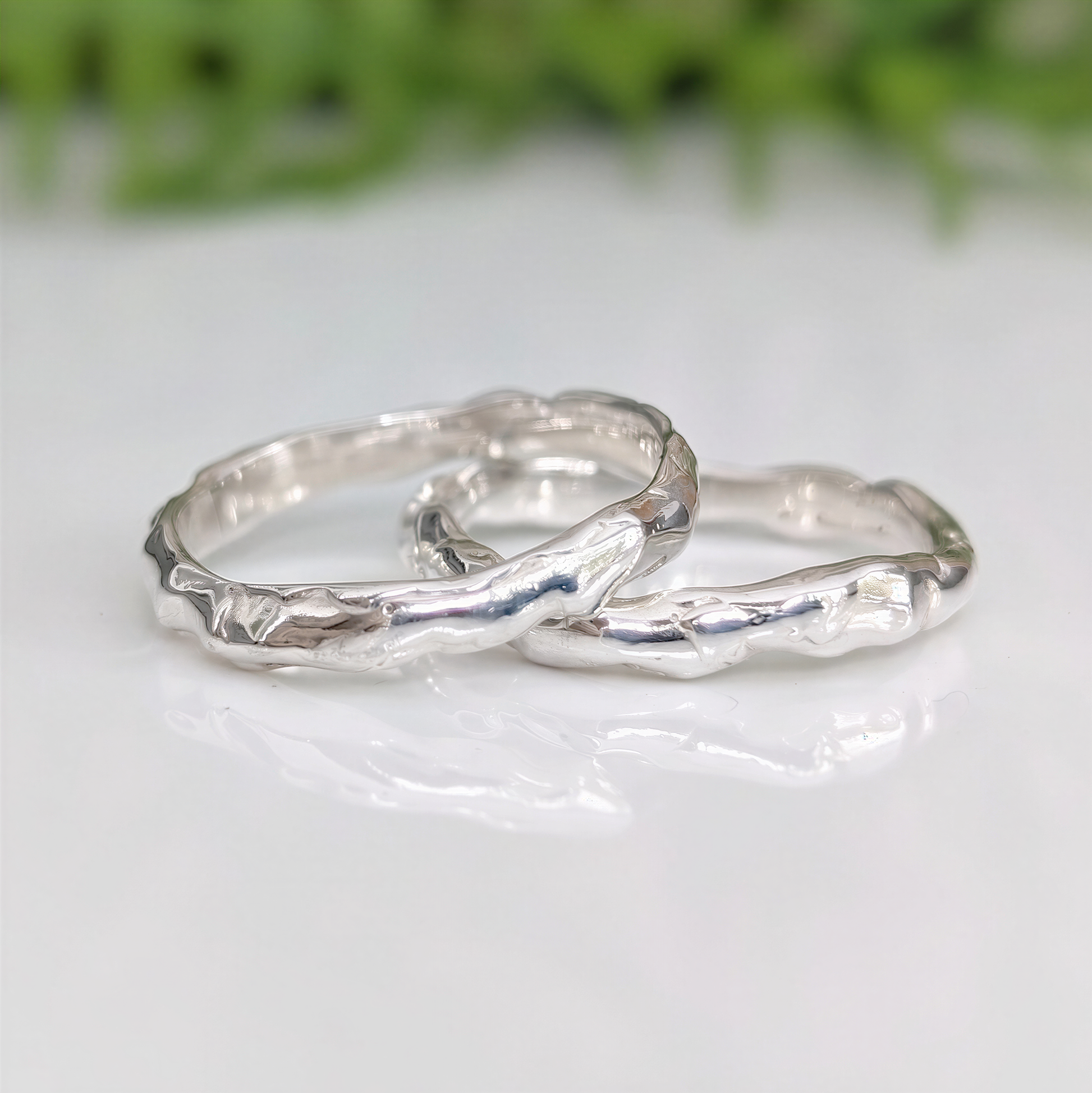 Two handcrafted Molten Silver wedding bands showcasing unique organic texture and elegance on a reflective surface.