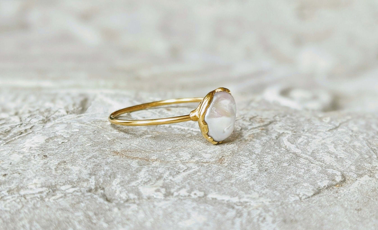 Handcrafted freshwater pearl ring on a textured stone surface, featuring a creamy-white Keshi pearl and a delicate gold band.