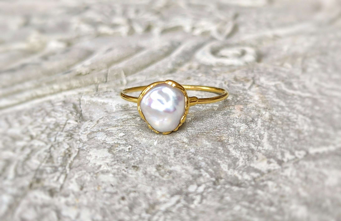 Delicate freshwater pearl ring on a textured surface, featuring a unique Keshi pearl set in gold.